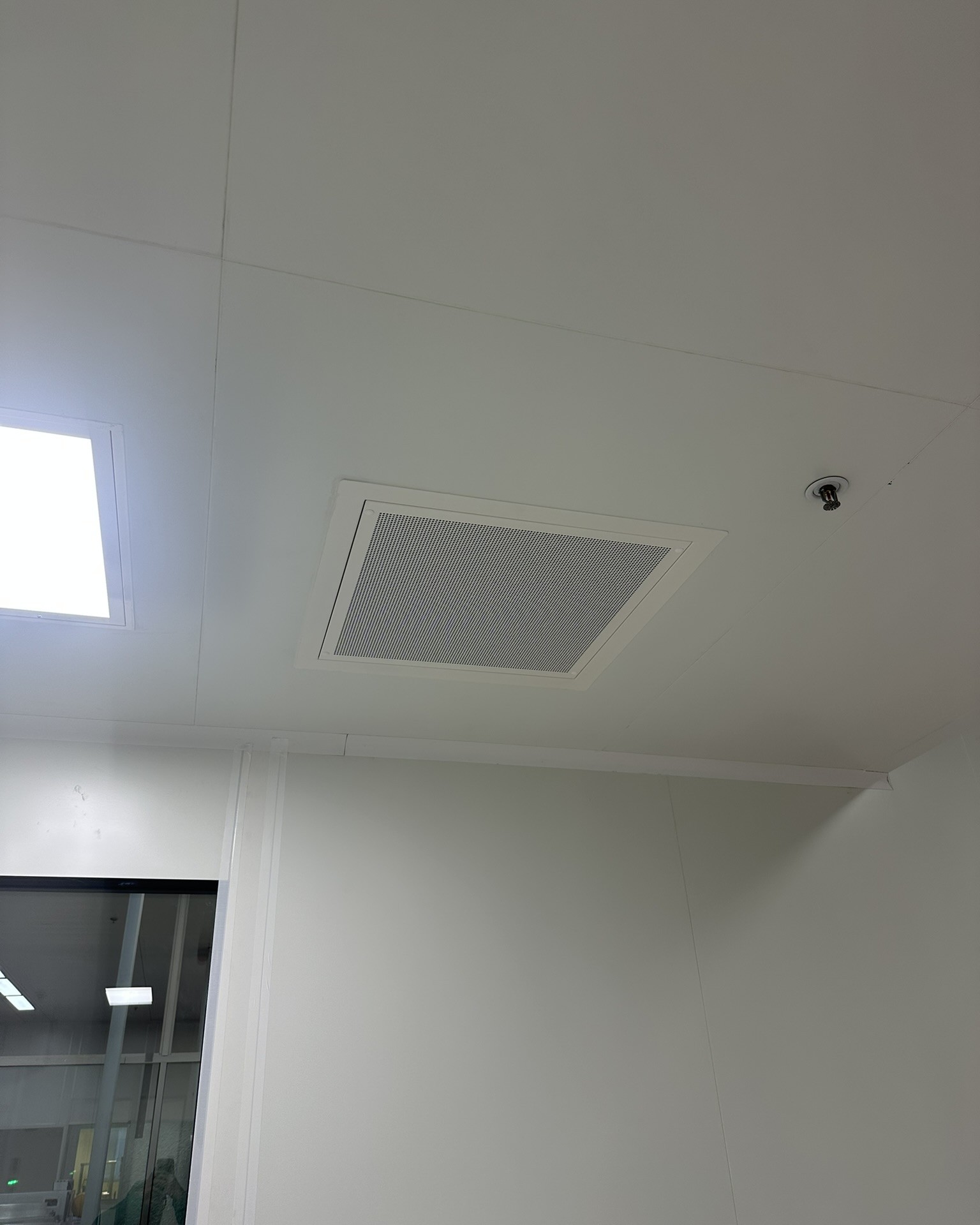 Diffuseur d'air rectangulaire intégré au plafond, à proximité d'un plafonnier lumineux en salle propre