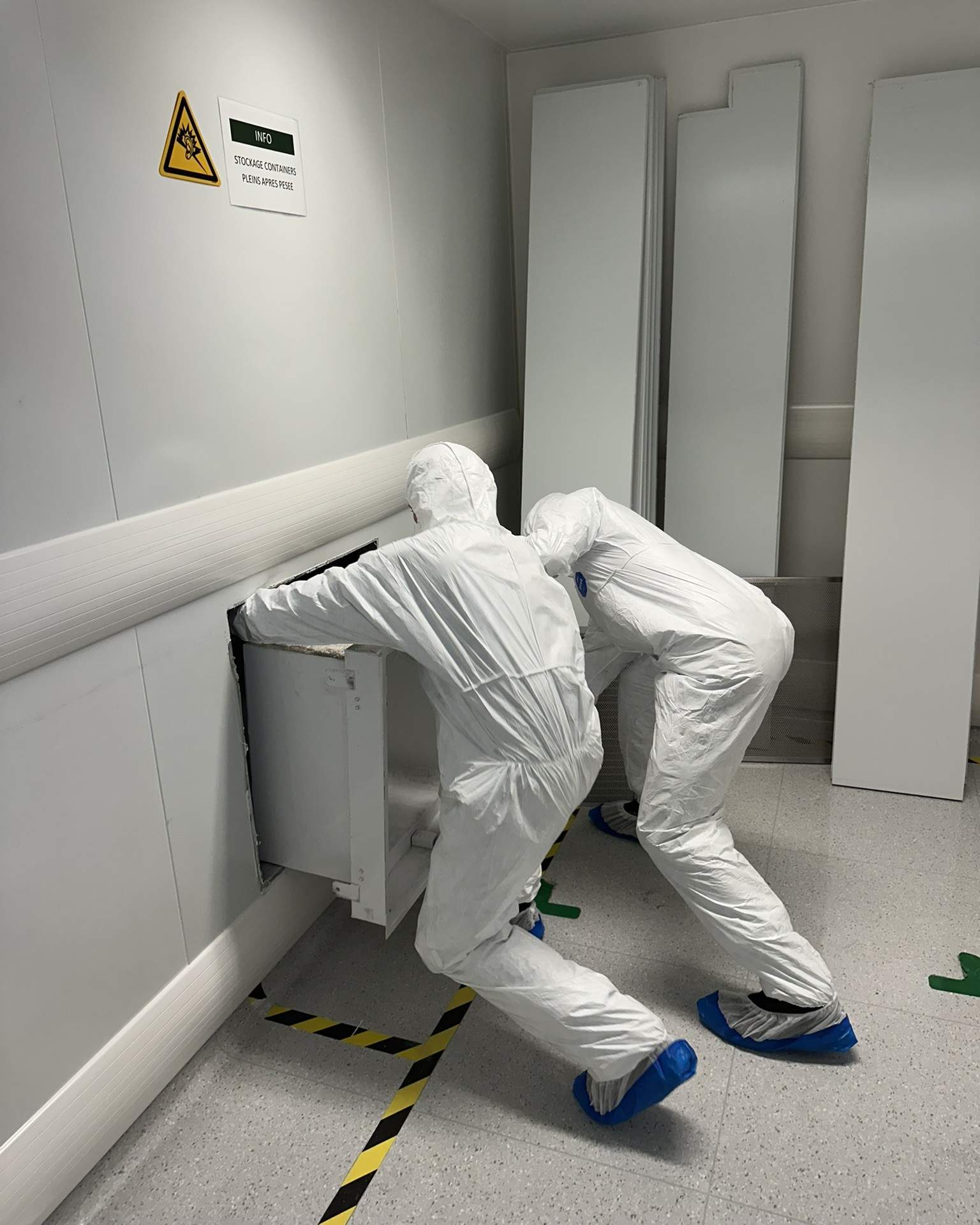 Deux techniciens en combinaison de protection intervenant sur un caisson technique en salle propre pharmaceutique